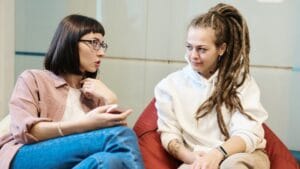 Two women engaged in a conversation in a modern office, sitting comfortably in relaxed chairs.