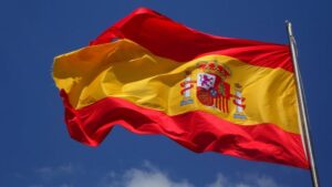 Vibrant Spanish flag waving against a clear blue sky and clouds.