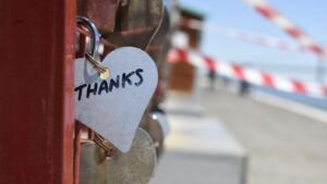 A heart-shaped love lock with 'THANKS' inscribed, hanging on a fence, symbolizing gratitude.